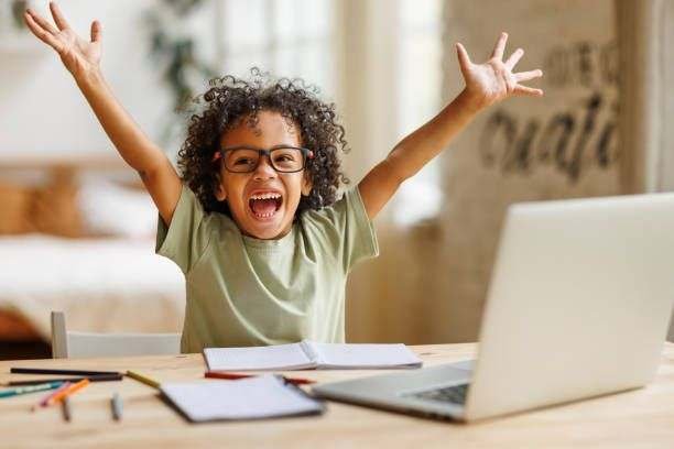 Un enfant lève les bras de joie devant son ordinateur